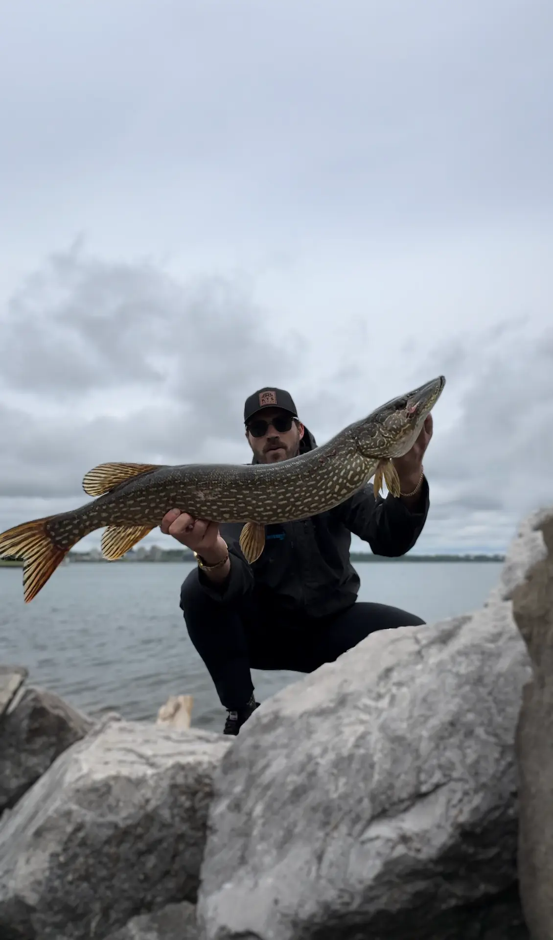 TJ LeClair holding a northern pike along a rocky shoreline
